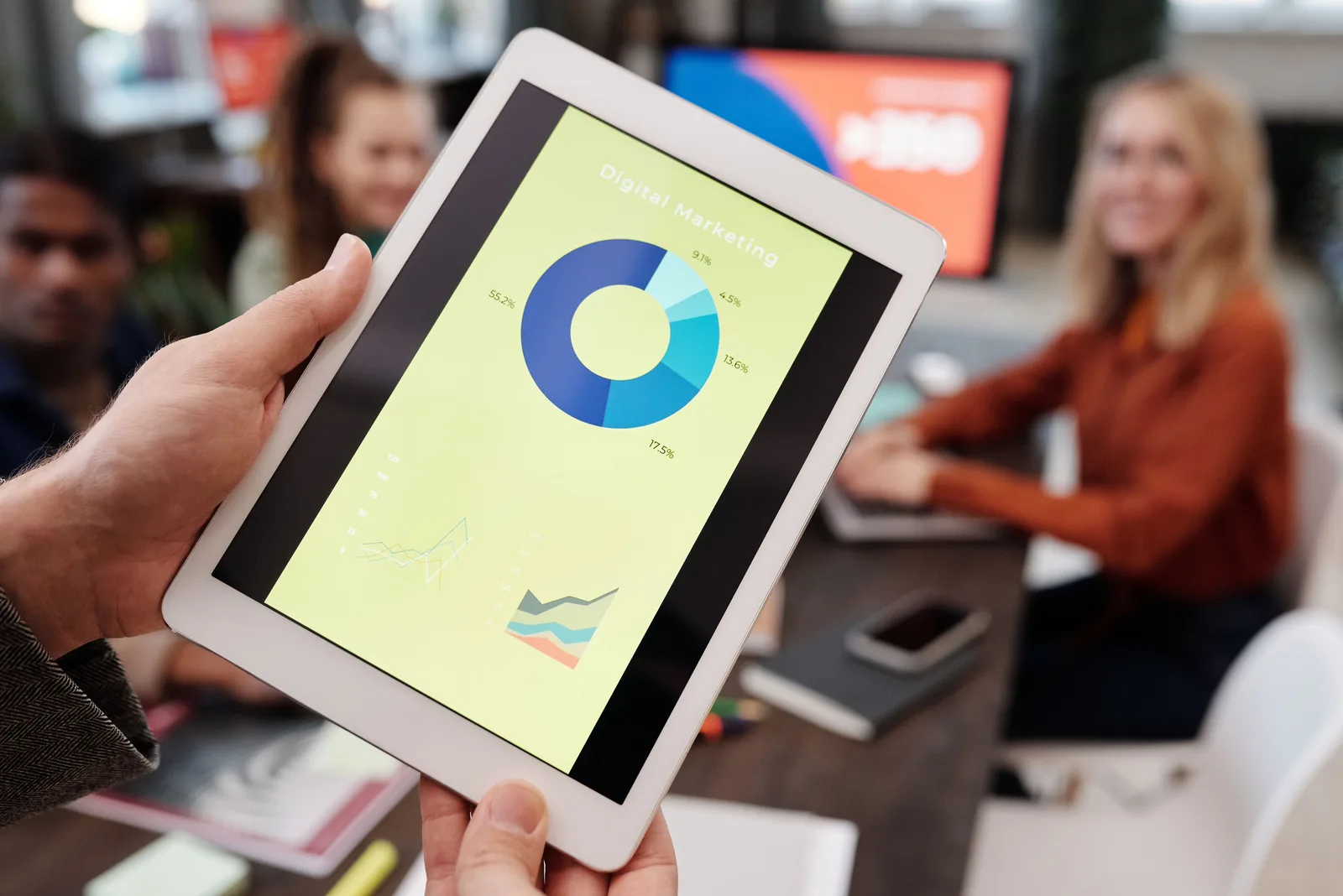 Business team reviewing digital marketing statistics on a tablet during an indoor meeting. Programmatic advertising tools: DV360, The Trade Desk, Amazon DSP, Google Ads and Xandr
