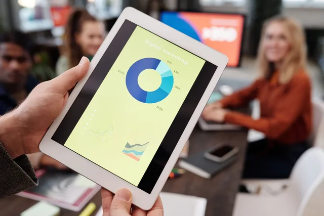 Business team reviewing digital marketing statistics on a tablet during an indoor meeting. Programmatic advertising tools: DV360, The Trade Desk, Amazon DSP, Google Ads and Xandr